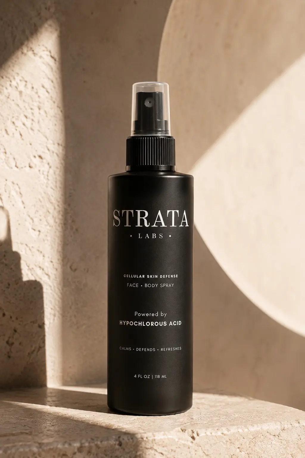 STRATA hypochlorous acid mist bottle, matte black with cream label on travertine stone